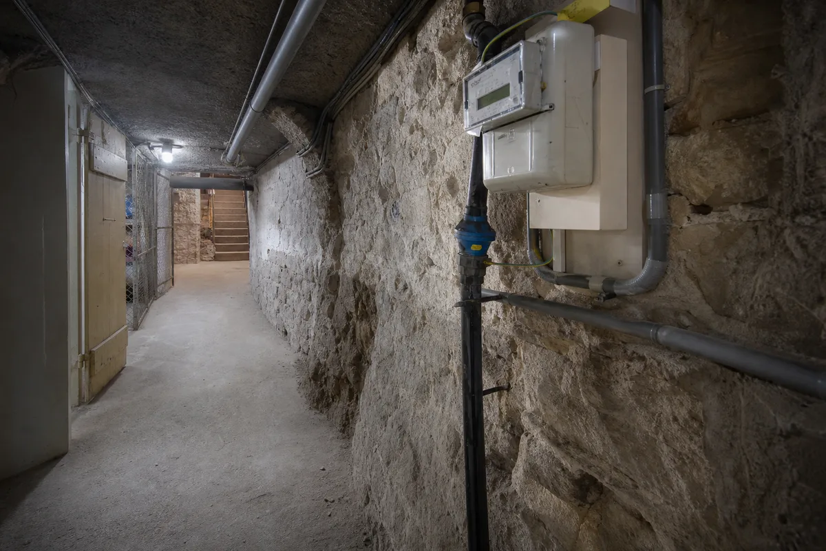 Cave et pied de mur d&rsquo;un immeuble parisien ancien, sol brut et canalisations