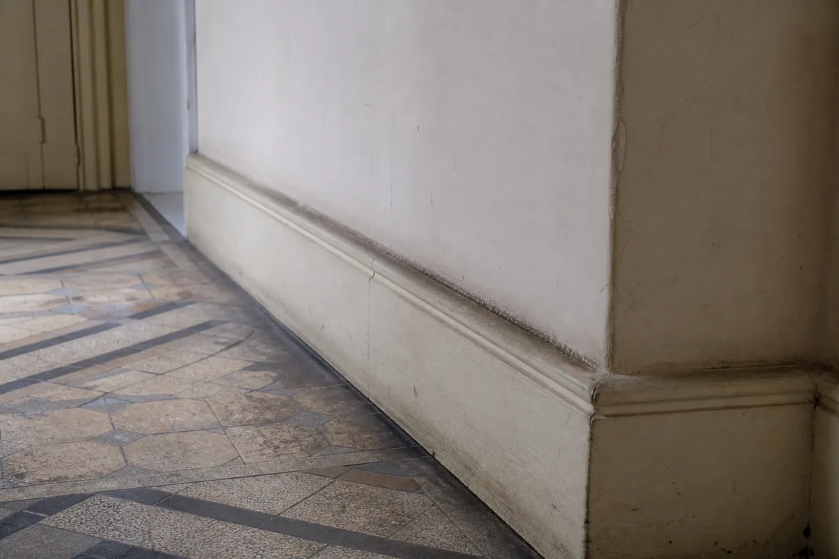 Plinthe et angle de mur d’un couloir d’immeuble ancien, traces le long du sol